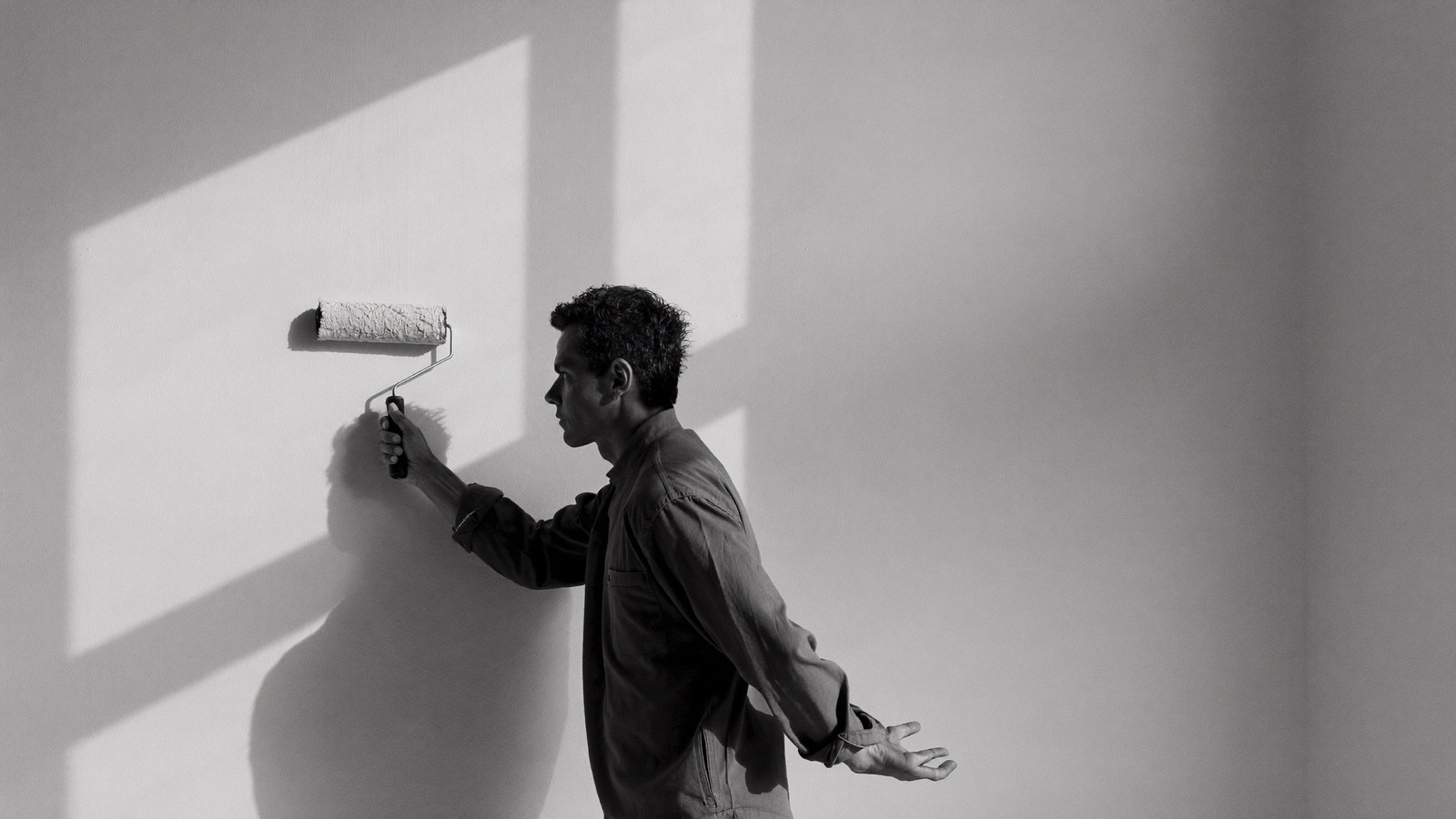 A painter rolling a fresh coat onto a wall in soft window light