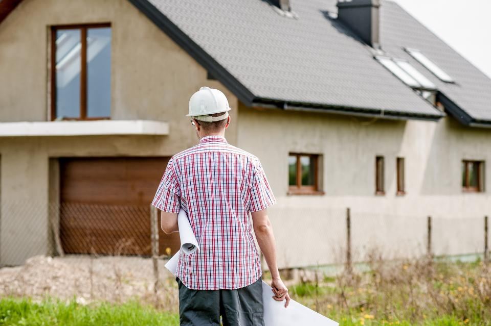 A builder with plans walking up to a house under construction