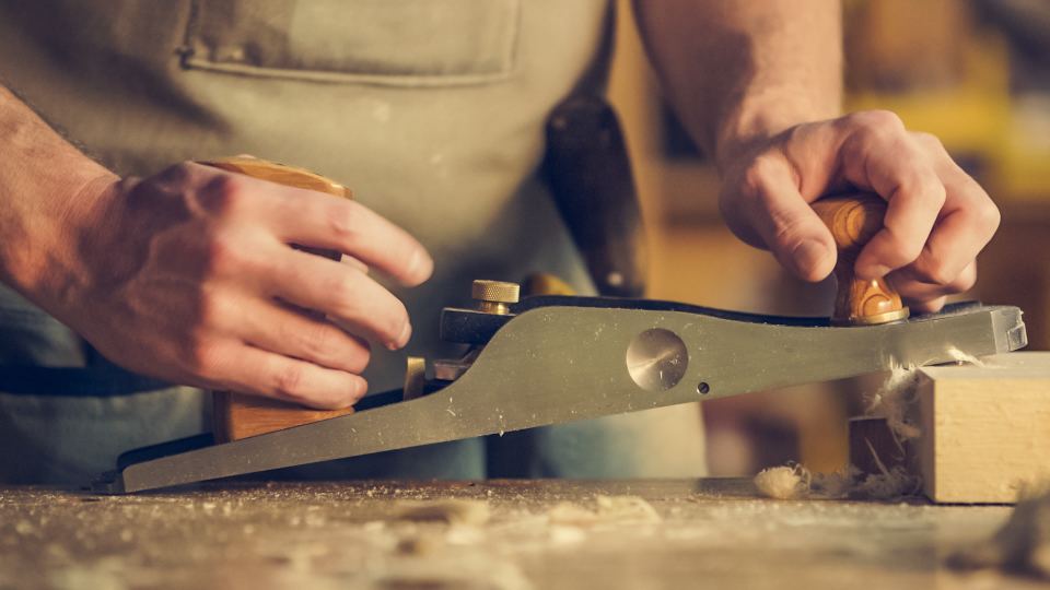 A carpenter's hands guiding a hand plane along timber