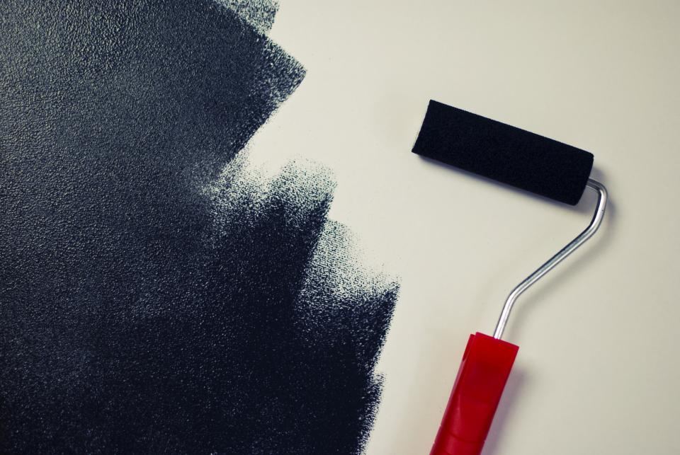 A paint roller beside a freshly rolled dark wall